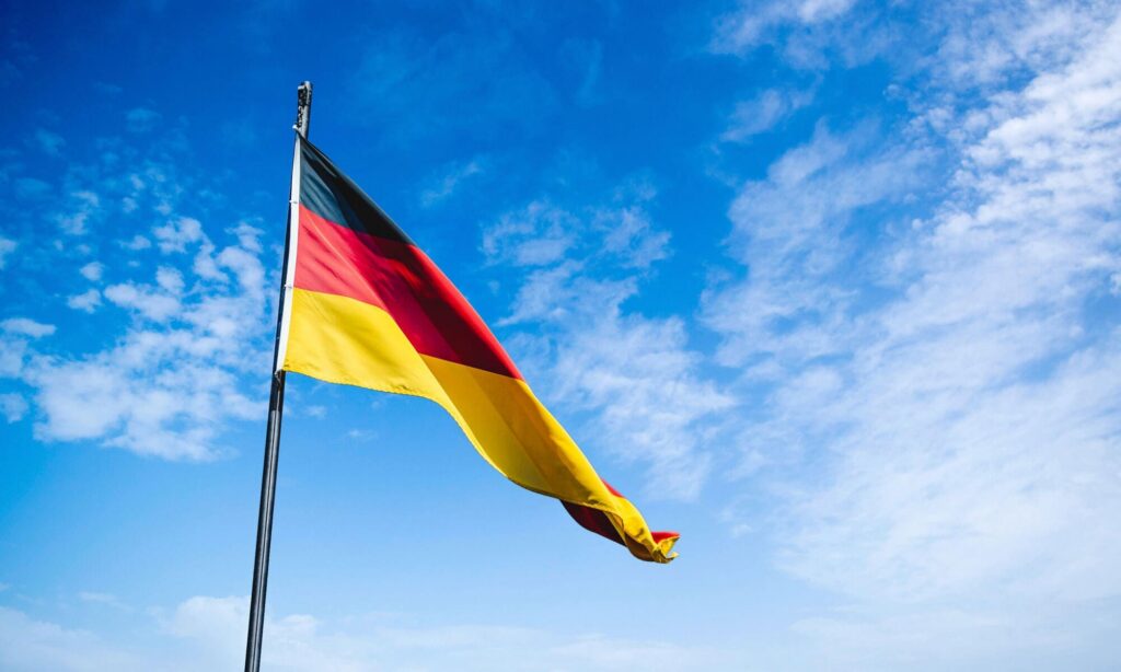 Deutsche Flagge in Schwarz-Rot-Gold weht im Wind an einem Fahnenmast vor blauem Himmel mit Wolken